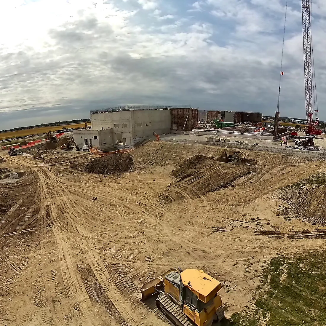 Daytime overview of an excavated site with plant working, from a mast-mounted camera
