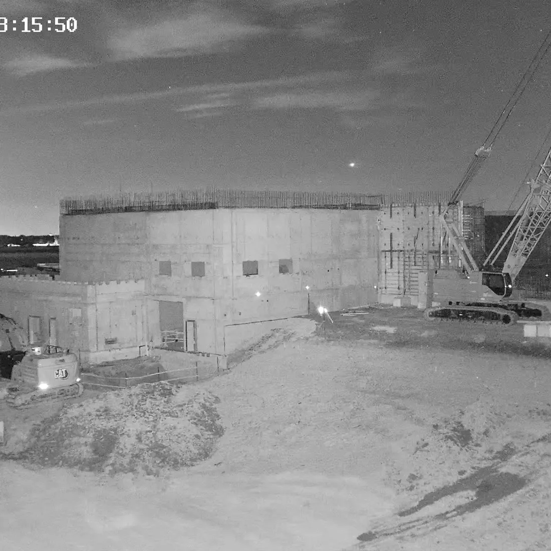 Night view of a concrete structure and crawler crane under site lighting