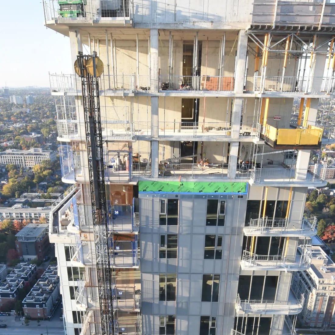 High-rise tower under construction above a city neighbourhood, formwork and a hoist on the face