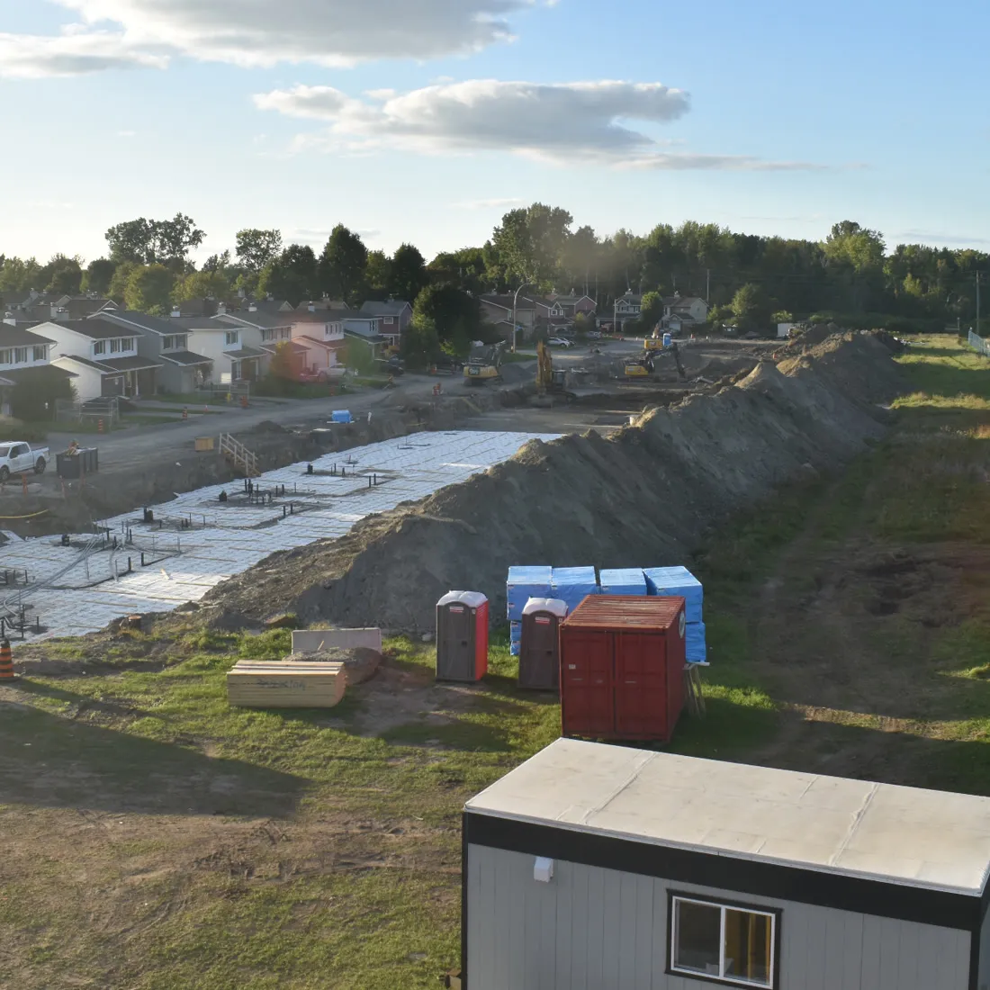 Excavated site with a site trailer and services laid in, beside a residential street