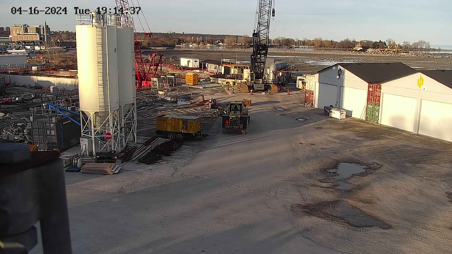 LSS camera view of a concrete batch plant with silo, crane and site buildings under early-evening light