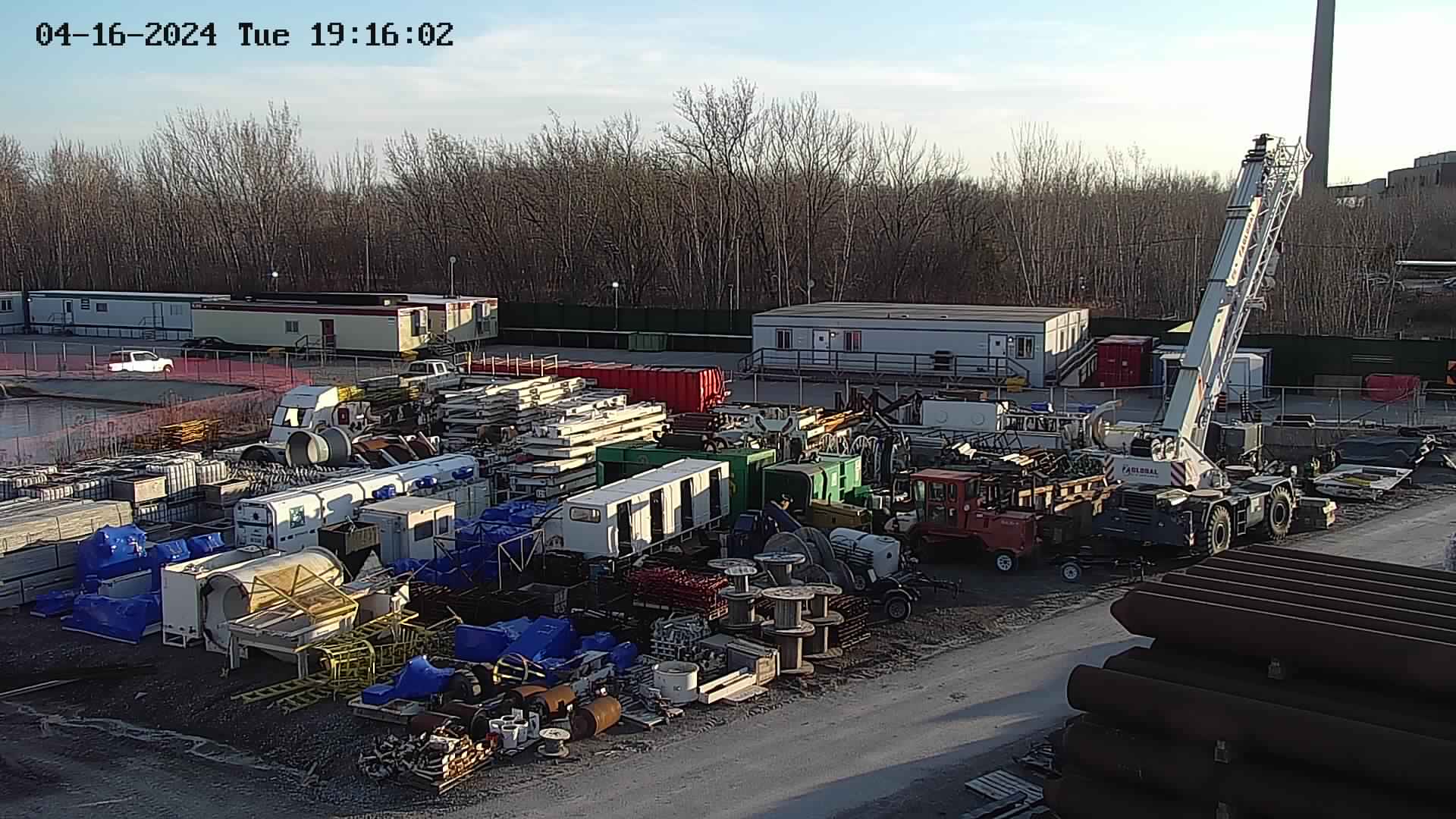 LSS camera view across a wide equipment laydown yard at dusk with containers, plant and a crawler crane
